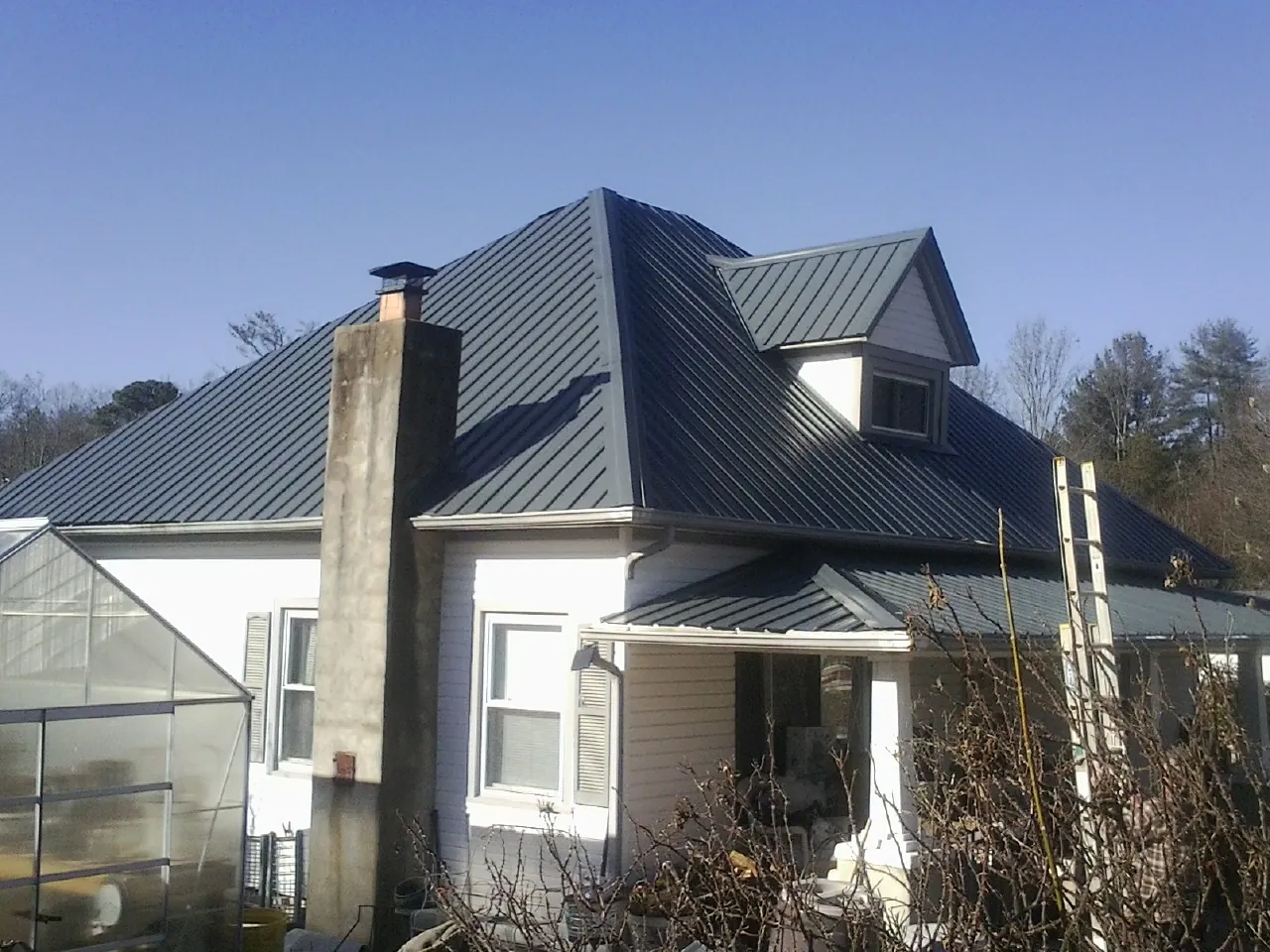 Dark blue standing seam metal roof on a white farmhouse with dormer — Slate & Tile Roof Repair by Roofing Brothers in Millersburg